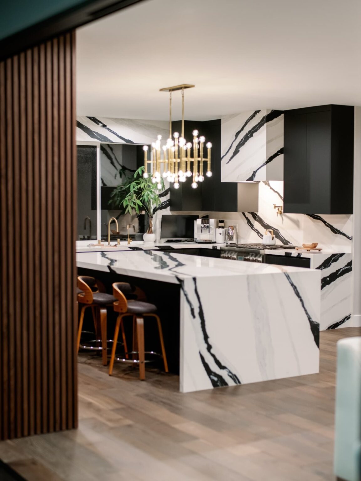 Kitchen with a marble waterfall island, walnut slat wall and brass chandelier in Tarzana by Home Deco