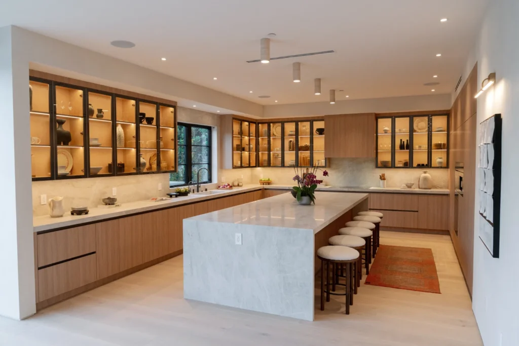 Open-concept kitchen with lit glass-front cabinets and a stone island in Studio City by Home Deco